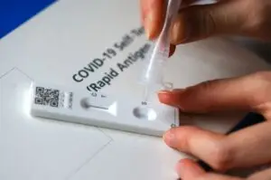 Person applying liquid sample to a COVID-19 rapid antigen self-test cassette.