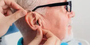 Audiologist fitting a modern hearing aid on a senior man wearing glasses