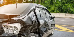 Black sedan with severe rear-end and side damage from a car accident on a highway