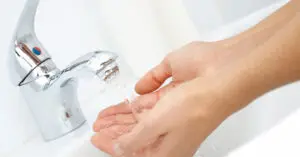 Person washing hands under a running chrome faucet
