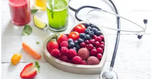 Heart-shaped bowl filled with fresh berries alongside green juice and a stethoscope.