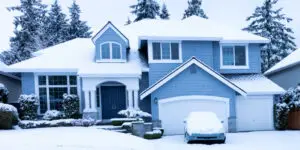 Blue suburban two-story house covered in winter snow with a car in the driveway