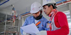 Two construction workers in hard hats reviewing blueprints on a job site.