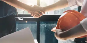 Construction engineer shaking hands with a client holding an orange hard hat and blueprints