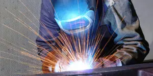 Industrial welder wearing protective helmet welding metal with bright sparks