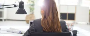 Businesswoman in grey blazer sitting at office desk facing laptop