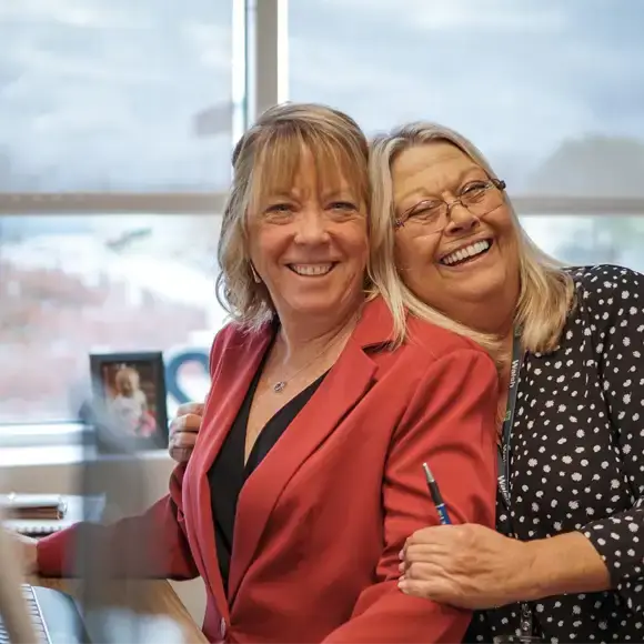 Two smiling female colleagues embracing in a professional office setting